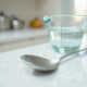 Cuillère en inox avec eau sur plan de cuisine blanc
